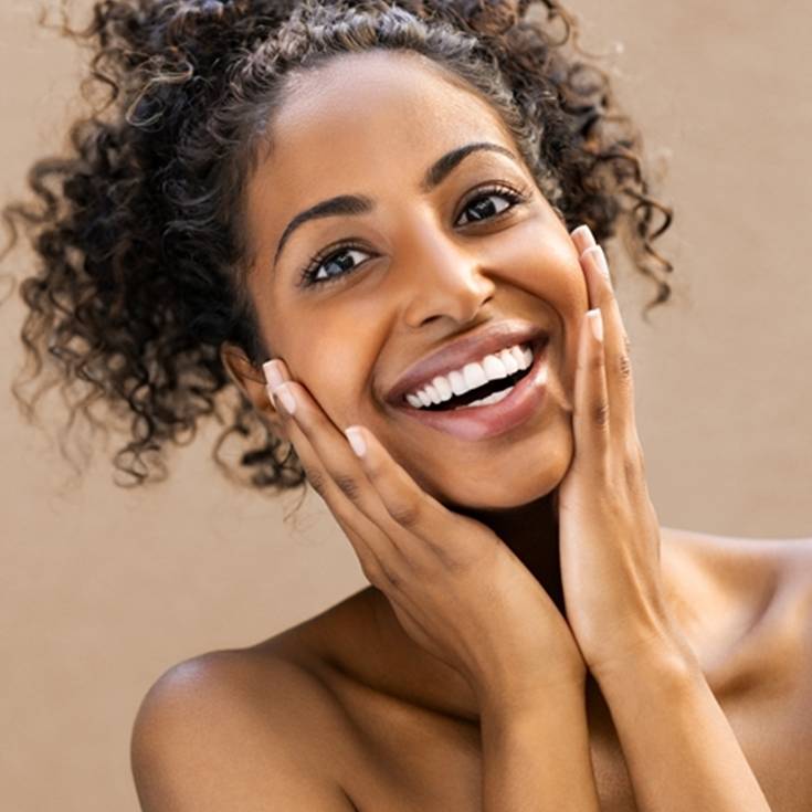 Imagem de mulher negra, sorridente, com as mãos no rosto.